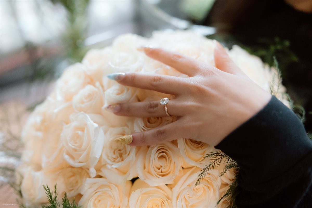 A hand resting on a white rose bouquet, showing an engagement ring