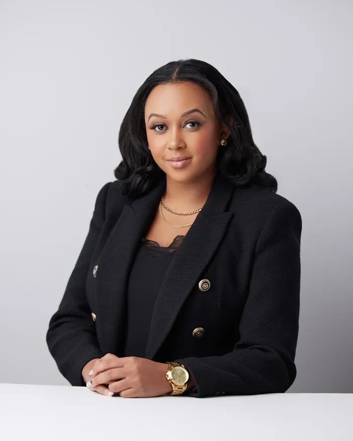 Toni Bullock seated in a black tweed blazer with gold buttons against a light grey studio backdrop